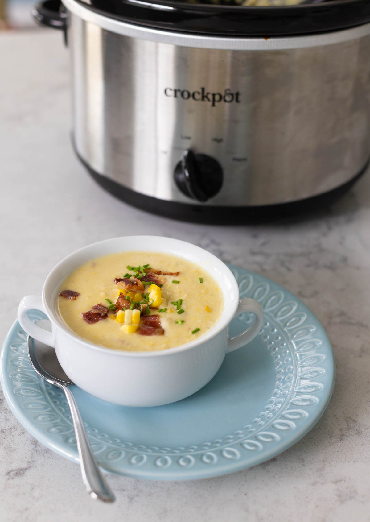 The serving of corn chowder is on the counter in front of the Crockpot