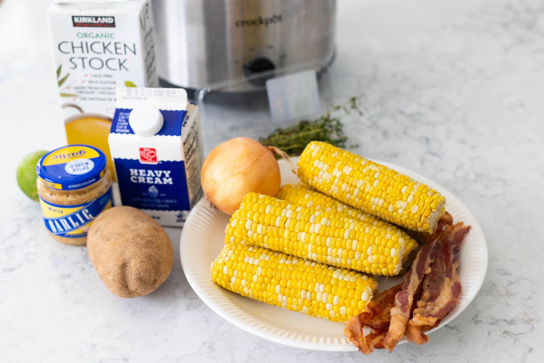 The ingredients to make the corn chowder from fresh corn on the cob are sitting on the counter in front of a Crockpot.