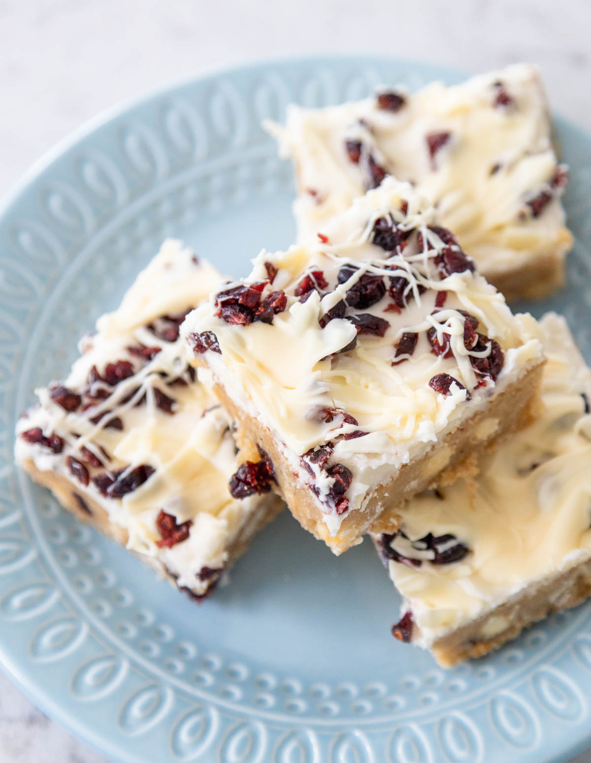 A blue plate has several cranberry bliss bars ready to serve, you can see the white chocolate drizzle on the tops.