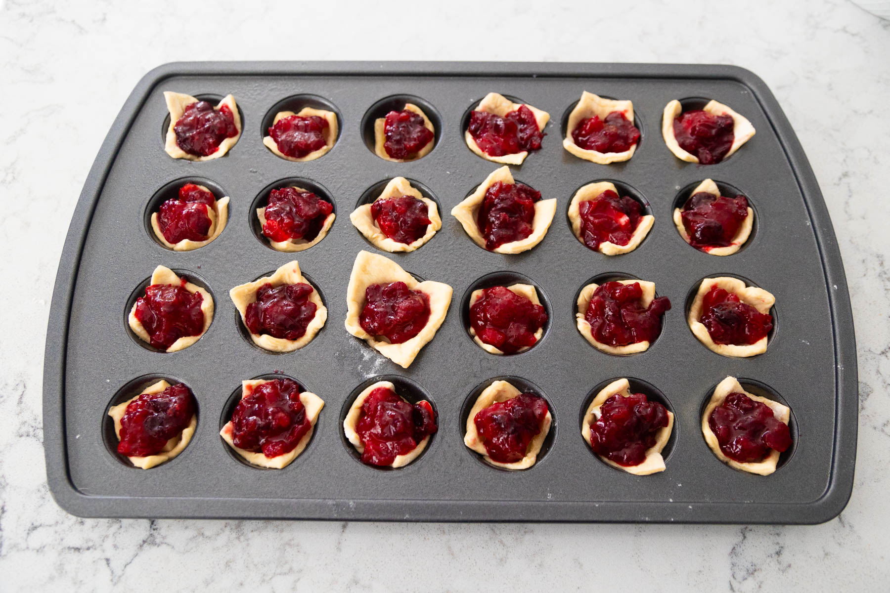 A tiny spoonful of cranberry sauce is added to each muffin tin well.