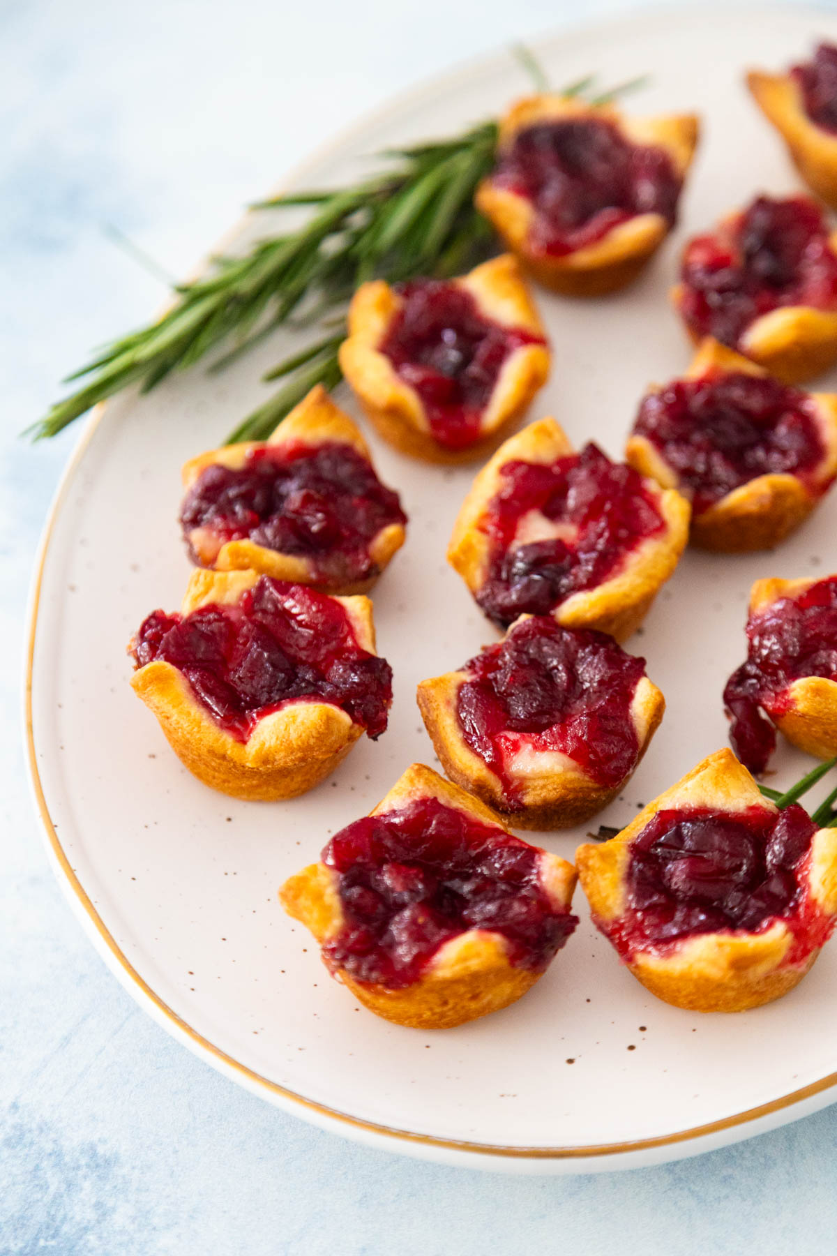 A platter filled with cranberry brie bites has a sprig of rosemary in the back.
