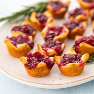 A platter filled with cranberry brie bites has a sprig of rosemary in the back.