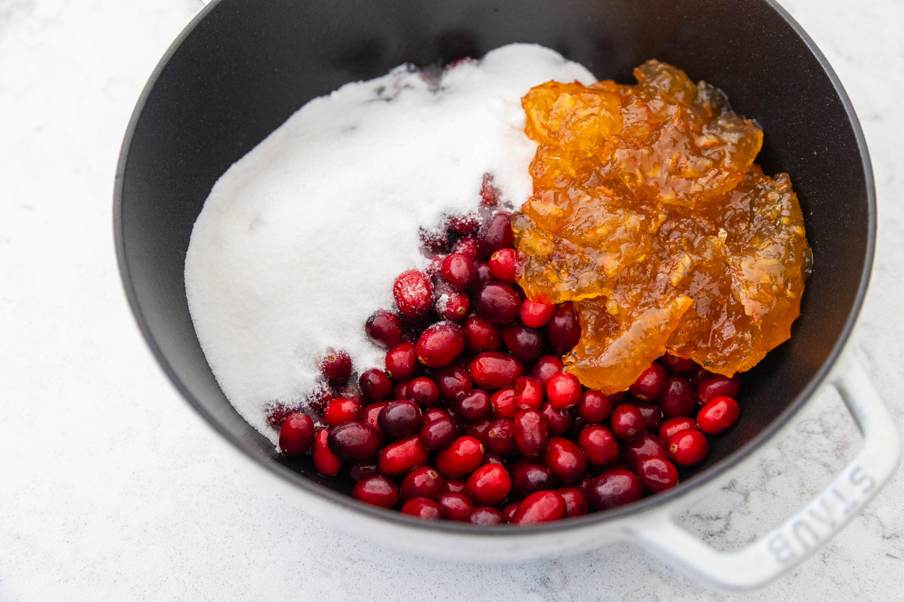The sugar, cranberries, and jam are in a large sauce pan.