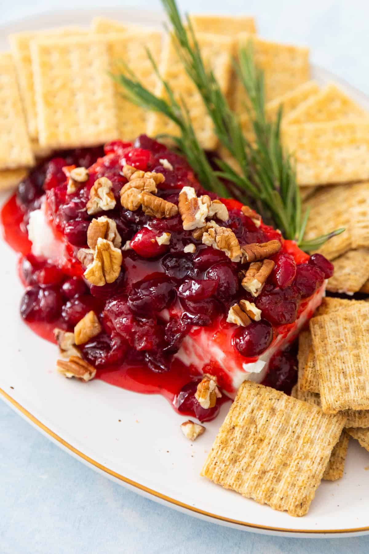 The cream cheese is on a platter with crackers. The cranberry sauce has been spooned over the top. Pecans have been sprinkled over.