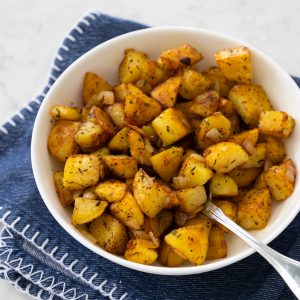 A white bowl is filled with golden brown home fries, delicious crispy breakfast potatoes.
