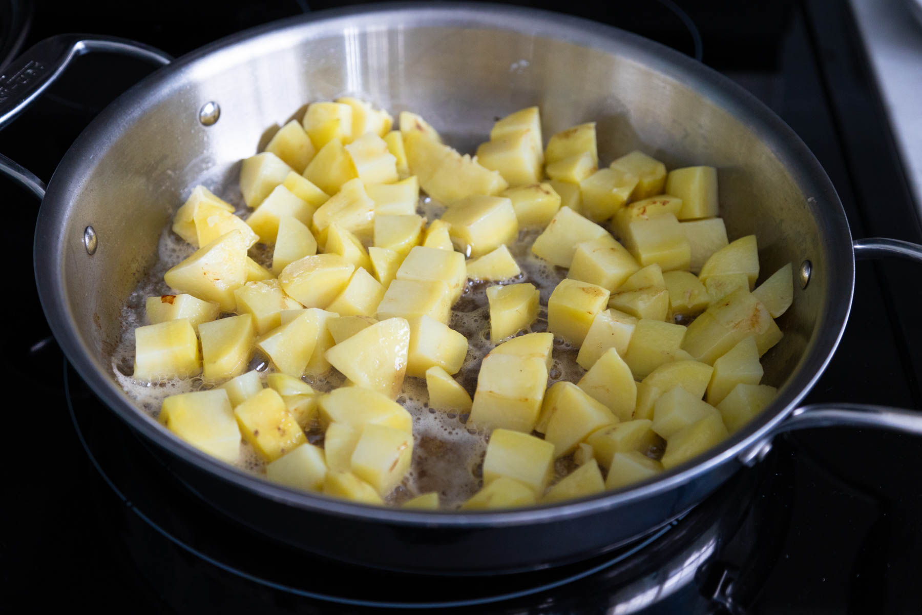 The potato chunks have been spread in an even layer in a large skillet.
