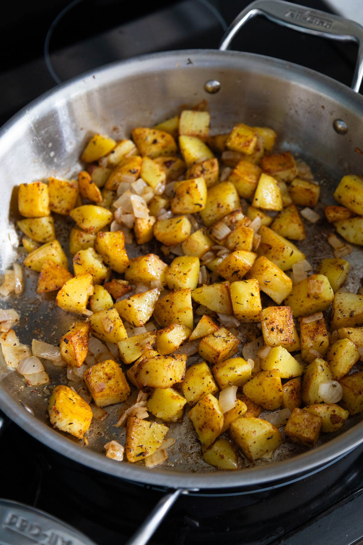 The crispy breakfast potatoes are in a skillet. They are golden brown and you can see the seasonings on top.