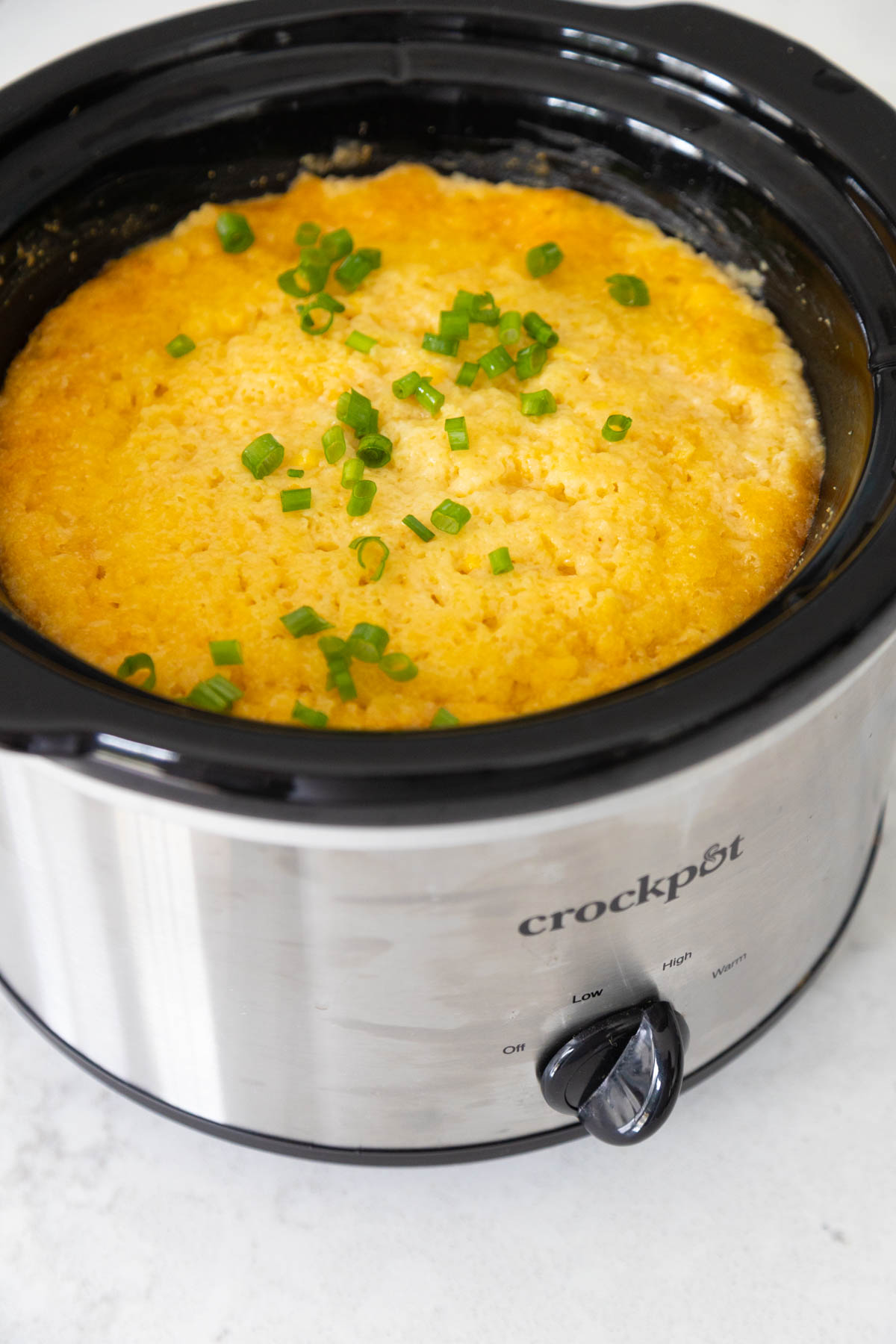 The finished corn casserole is in the Crock Pot and has chopped green onions over the top.