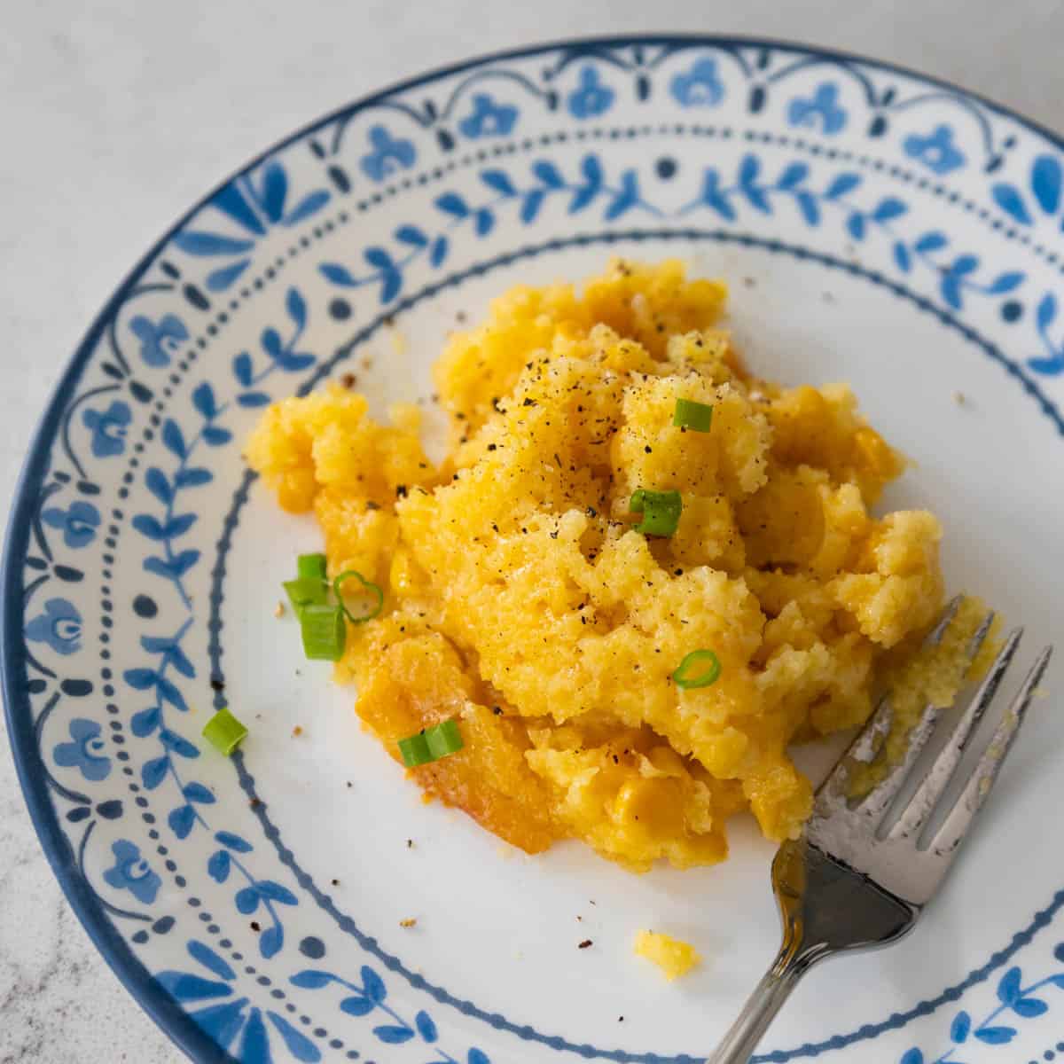 A scoop of the jiffy cornbread casserole is on a white plate with a blue decorative border.