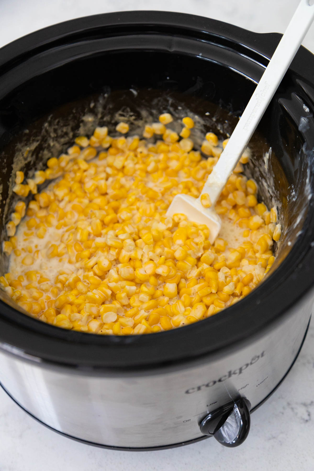 The creamed corn is finished and being stirred by a spatula in the Crock Pot.