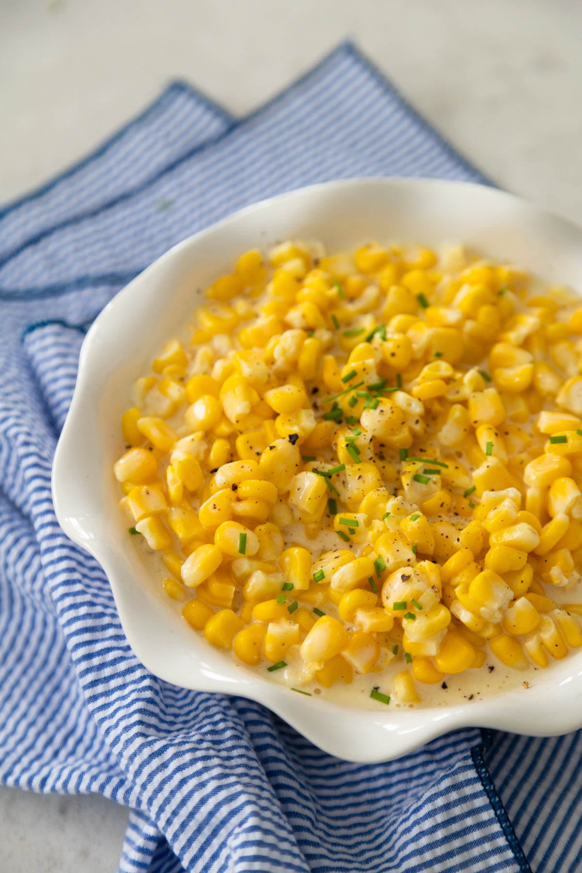 The serving bowl is filled with creamed corn and sits on a blue napkin.