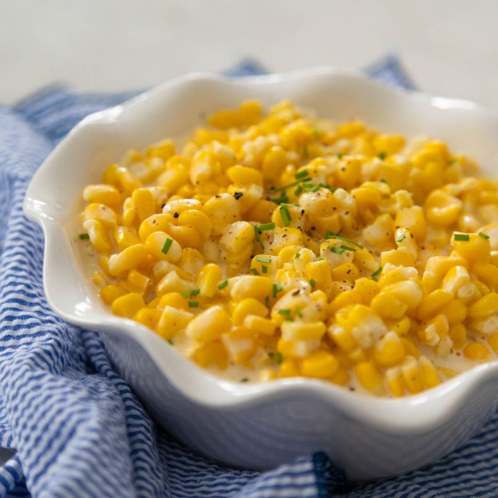 The white ruffled bowl has creamed corn made in the Crock Pot. Fresh chives are sprinkled over the top.
