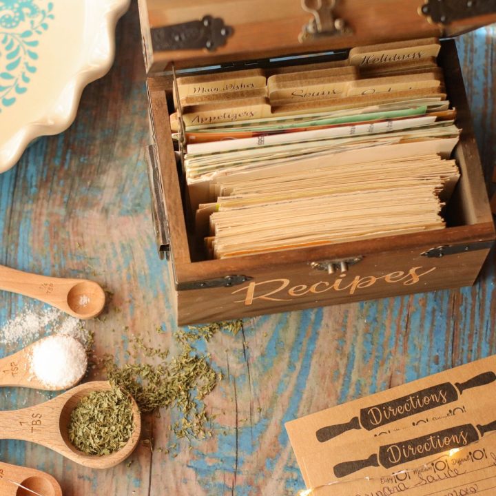 An old fashioned woodend recipe box is filled with recipe cards. Measuring spoons filled with salt and herbs are scattered around it.