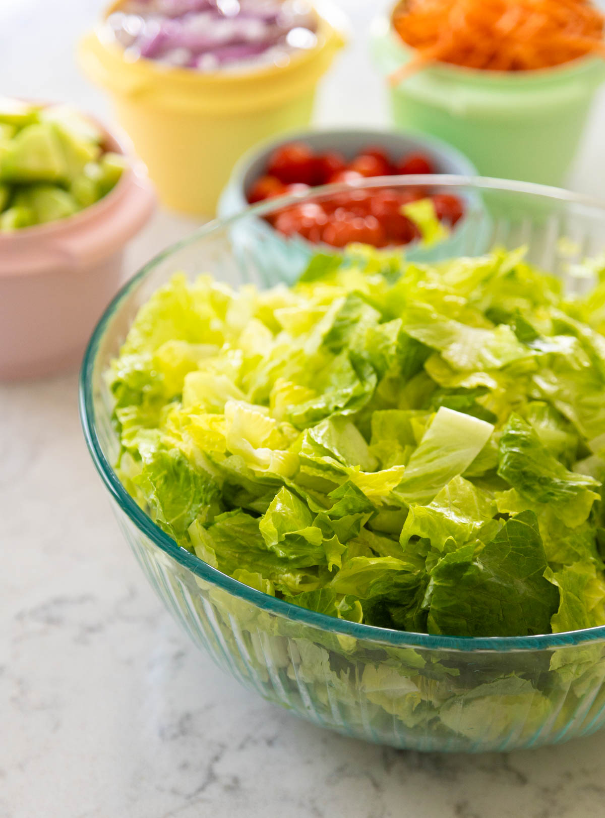A big bowl of chopped lettuce sits in front of the other vegetables in small bowls.