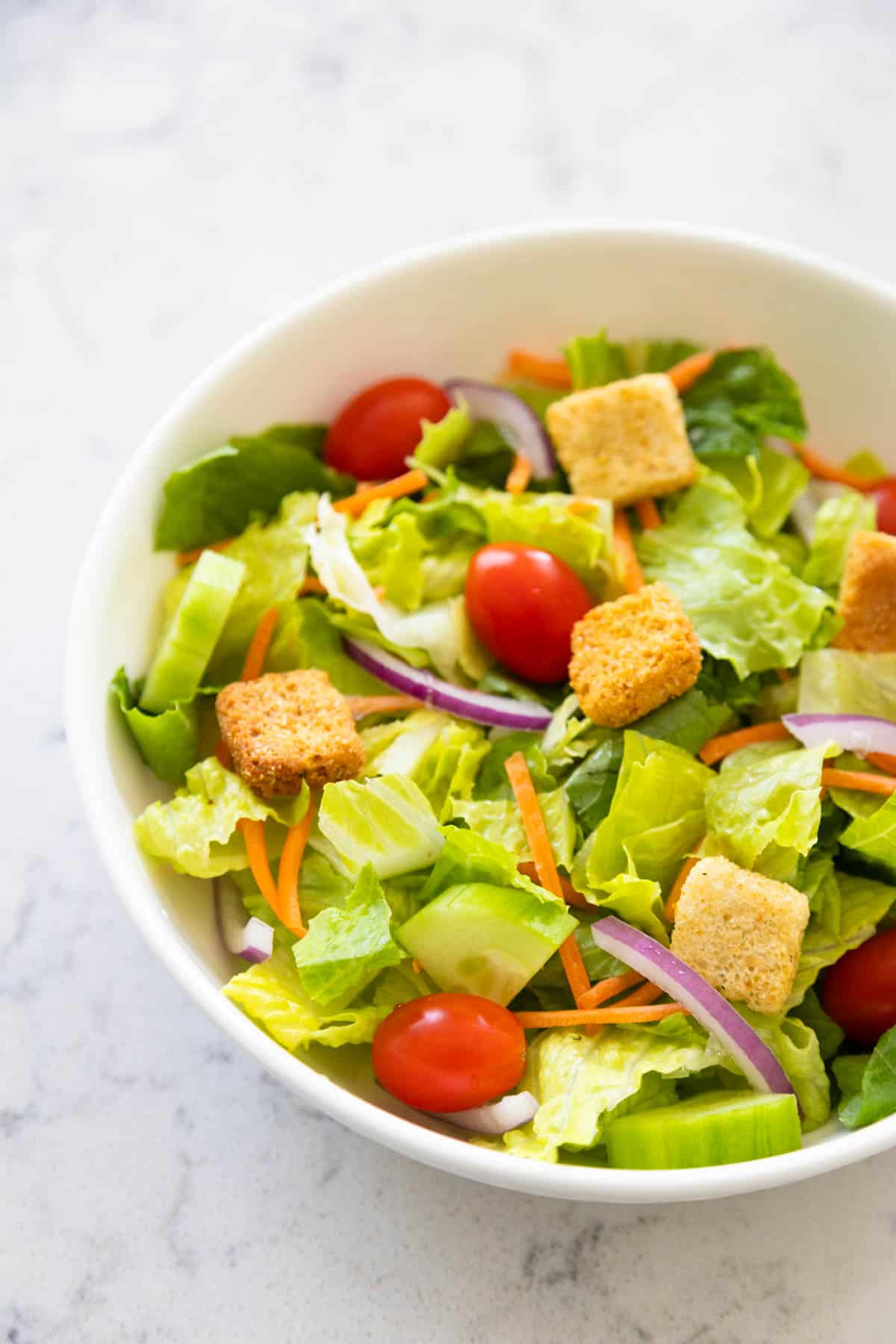 The salad is ready to be dressed and is in a white bowl.