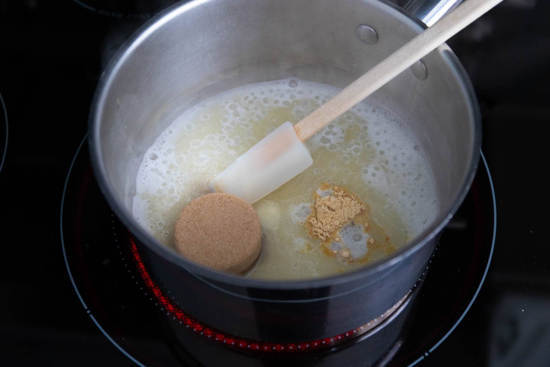 The butter has been melted in a saucepan, a scoop of brown sugar and some dried ginger have been added and are about to be stirred in.