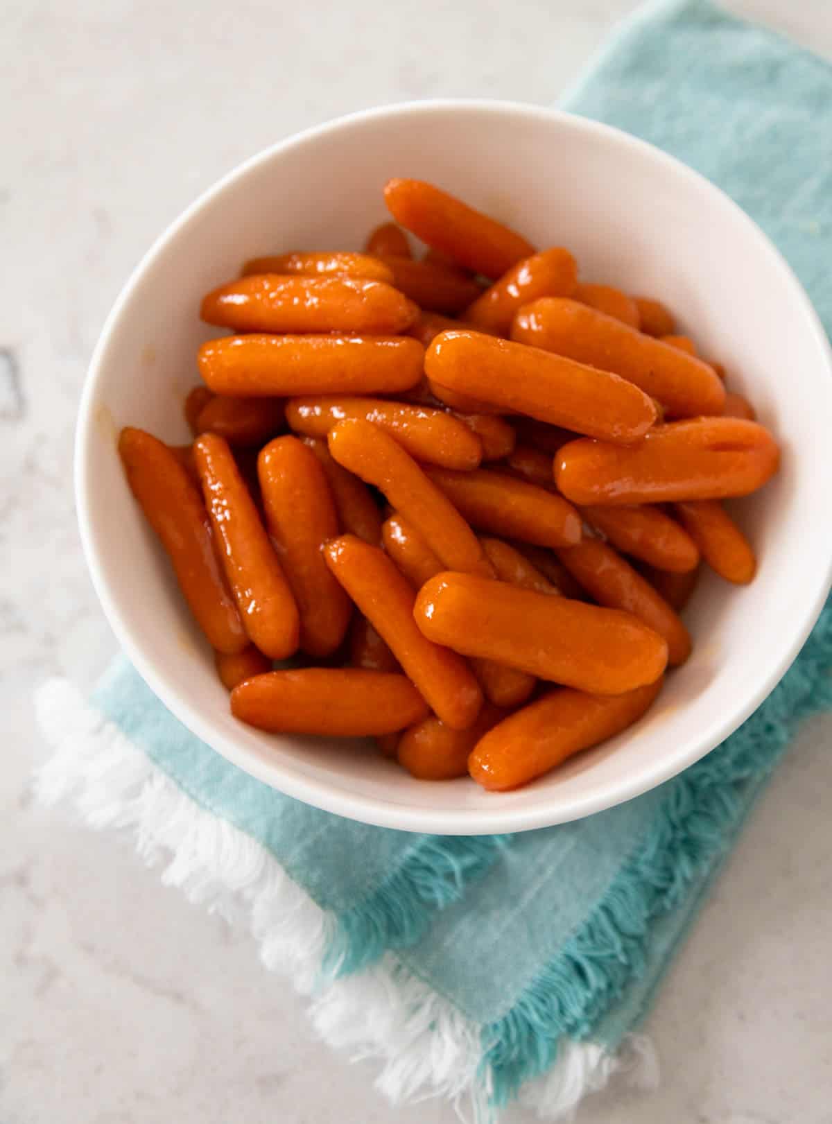 A white serving bowl is filled with the glazed baby carrots.