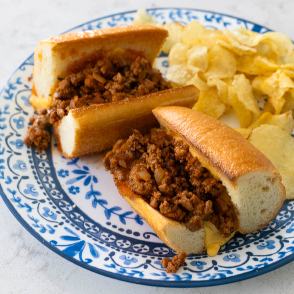 The baked ground turkey sloppy joes are on a blue plate with potato chips.