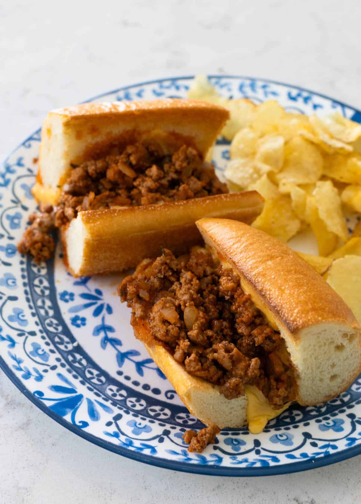 The baked ground turkey sloppy joes are on a blue plate with potato chips.