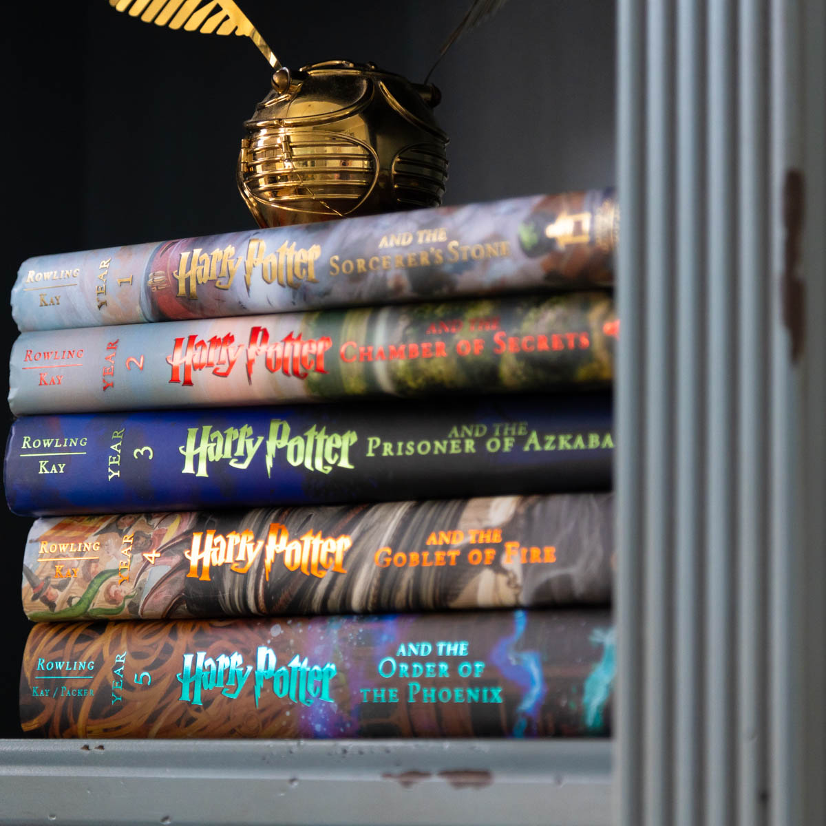 A stack of the Illustrated Harry Potter Books are on a shelf with a golden snitch sitting on top.