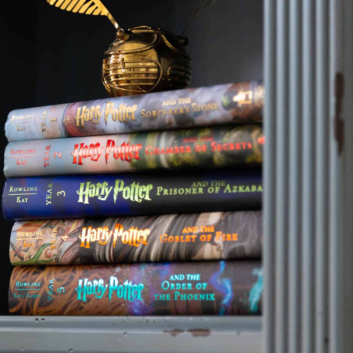 A stack of the Illustrated Harry Potter Books are on a shelf with a golden snitch sitting on top.