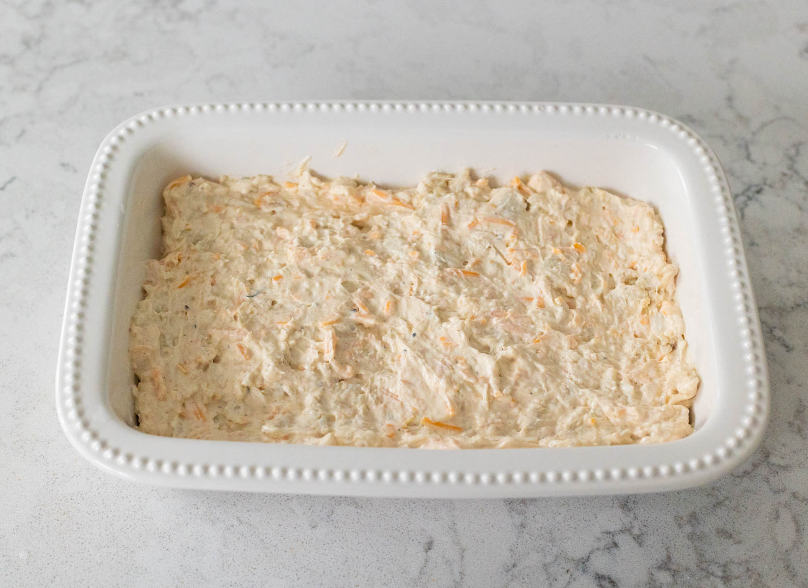 The white baking dish has a smooth layer of prepared crab dip.