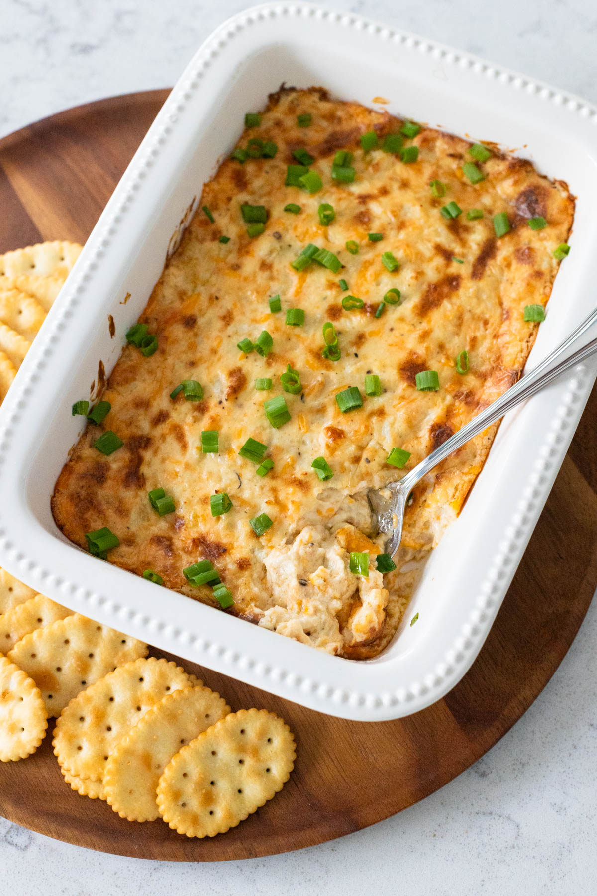 The baking dish of hot crab dip is being served on a platter with butter crackers.
