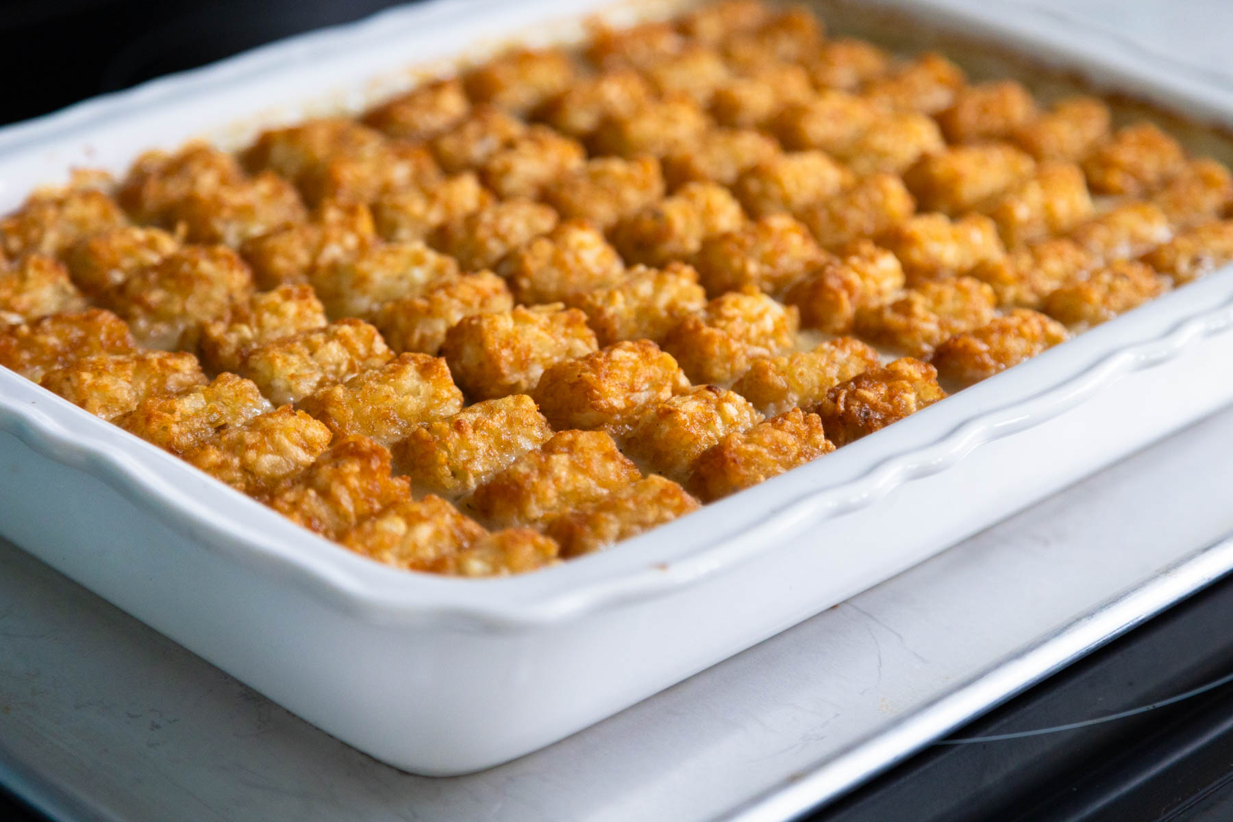 The assembled tater tot casserole is on a baking pan fresh out of the oven with golden brown tater tots on top.
