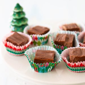 A Christmas platter is filled with squares of fudge in small festive cupcake wrappers for serving.