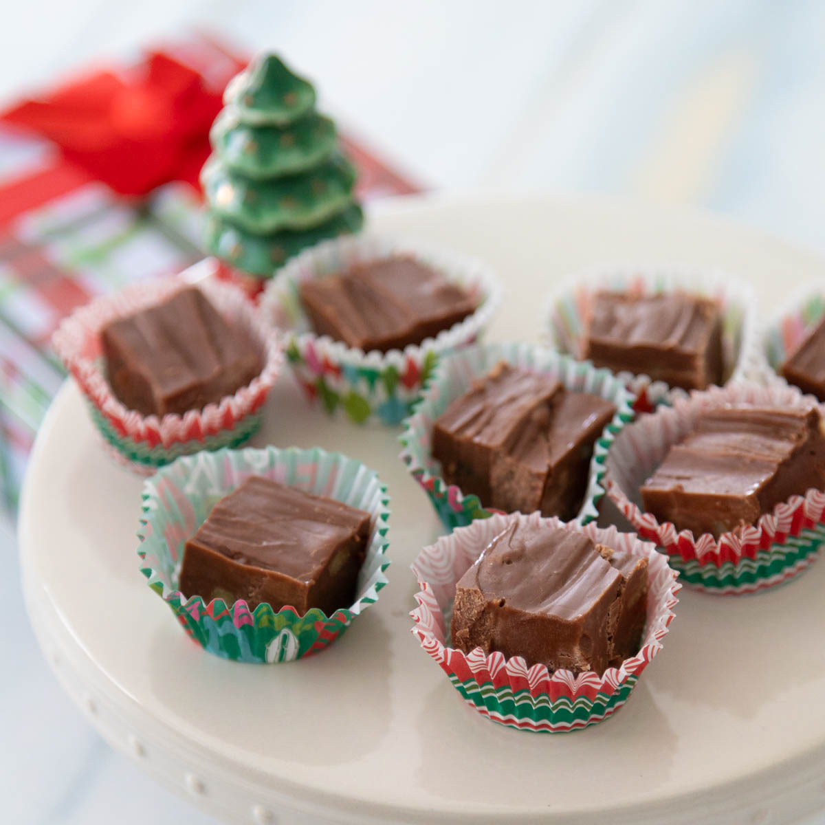 The squares of fudge are served on a pretty cake plate with a Christmas tree accent.