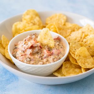 A bowl of sausage dip sits next to a plate of tortilla chips.