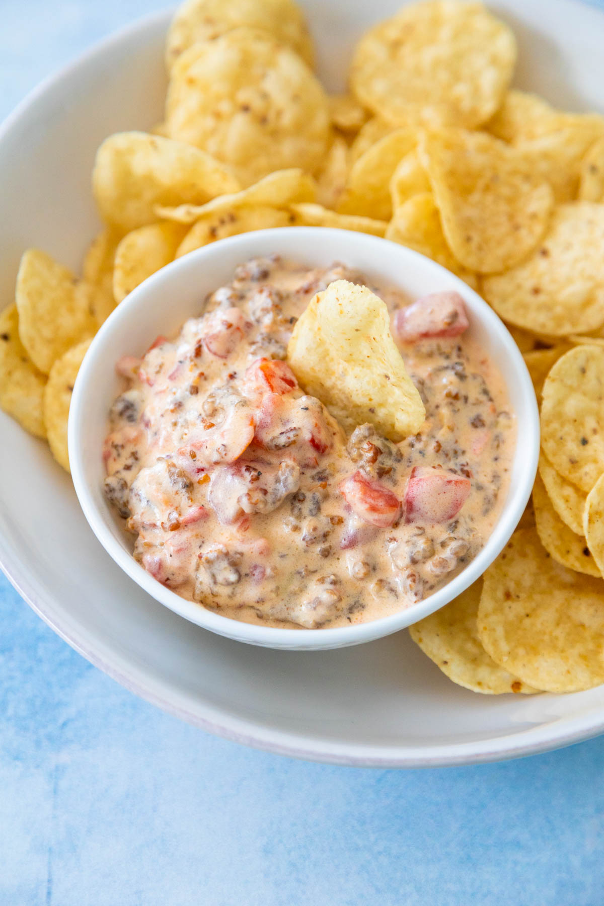 The sausage dip is in a bowl nestled inside a bowl of tortilla chips for serving.