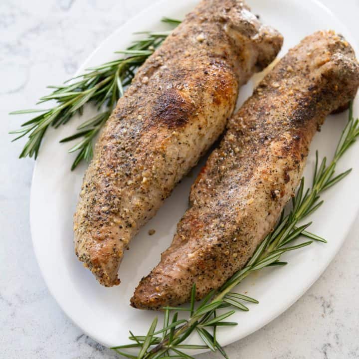 Two Smithfield pork tenderloins have been seasoned and roasted. They are now served on a white platter with fresh rosemary garnish.