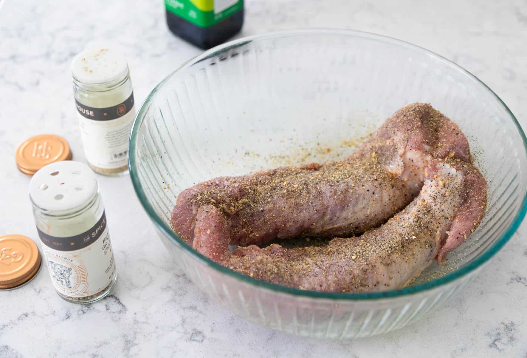 The pork has been added to a mixing bowl to be coated with olive oil and sprinkled with seasonings.