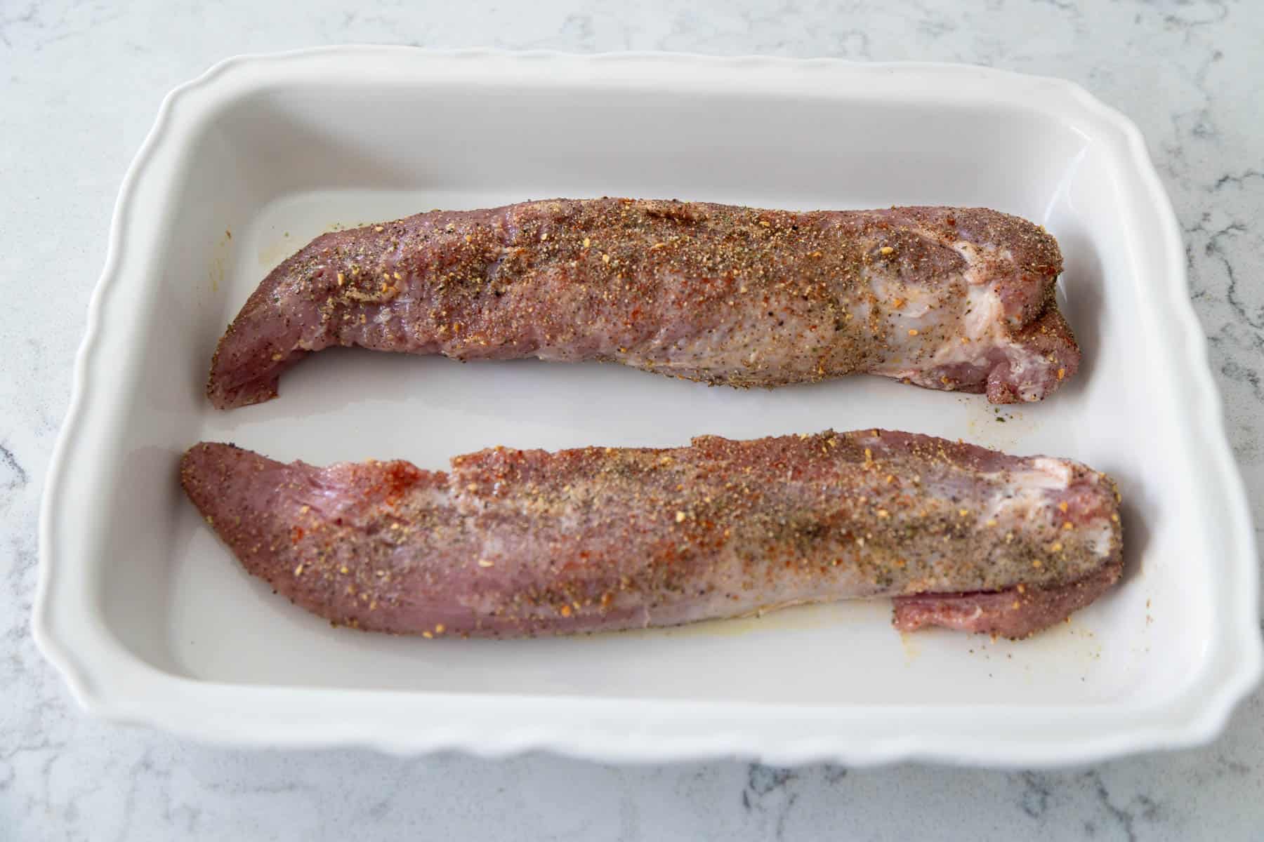 The pork tenderloins have been added to a white baking dish and are about to go in the oven.