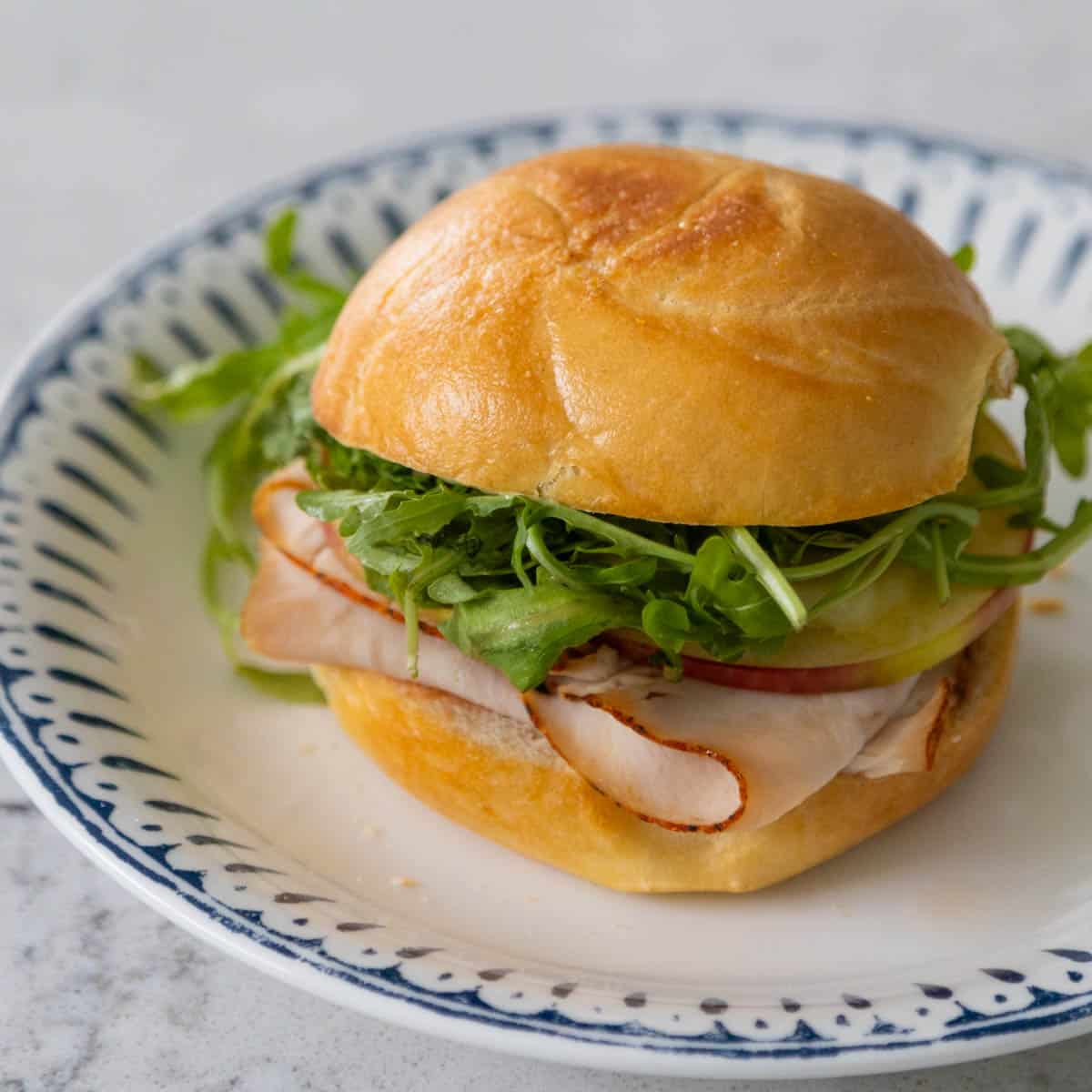 The finished sandwich is on a plate with a blue decorative border.