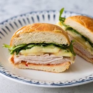 The baked turkey brie sandwich has been sliced in half so you can see the layers of turkey, apple, brie, and arugula.