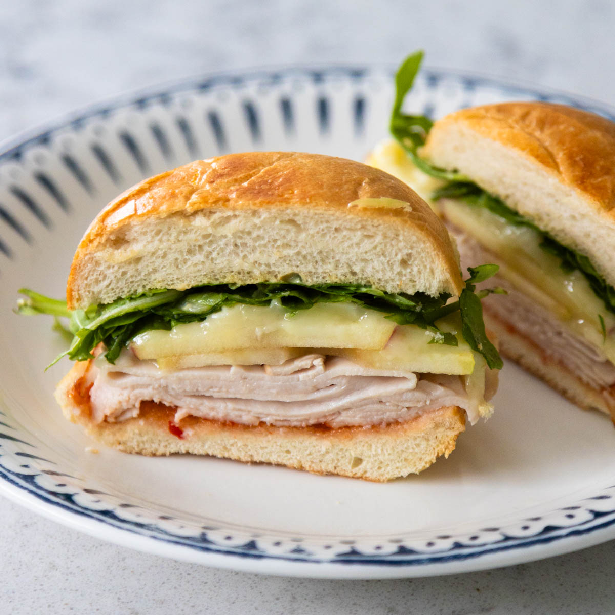 The baked turkey brie sandwich has been sliced in half so you can see the layers of turkey, apple, brie, and arugula.