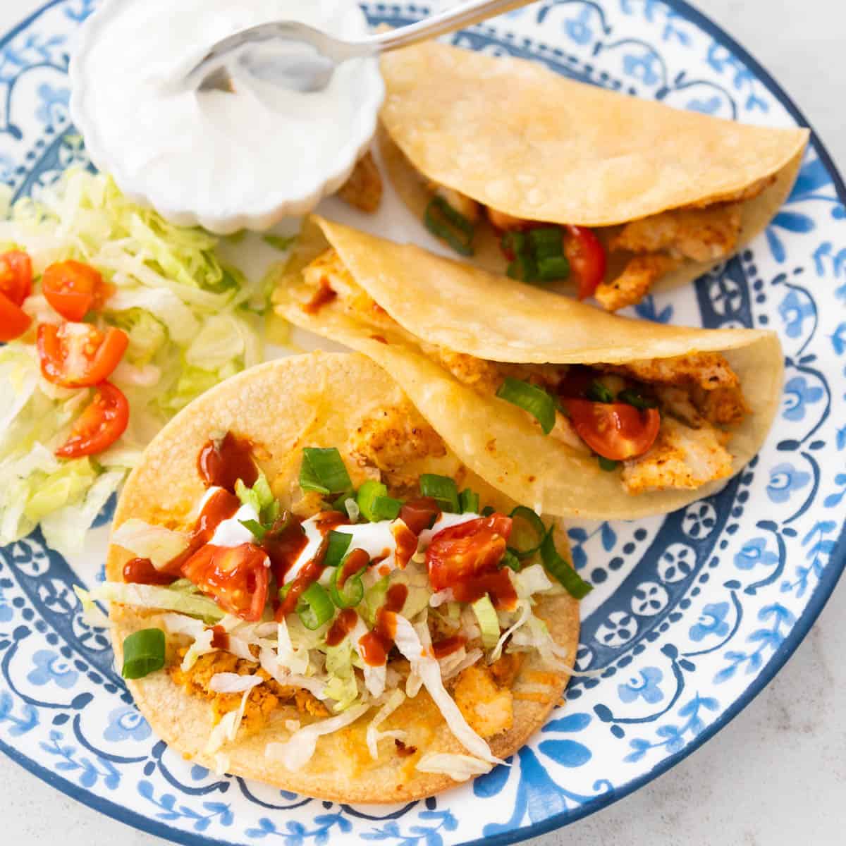 The dinner plate has several tacos on it, one is open wide so you can see the shredded lettuce, diced tomatoes, and taco sauce drizzled over the top.