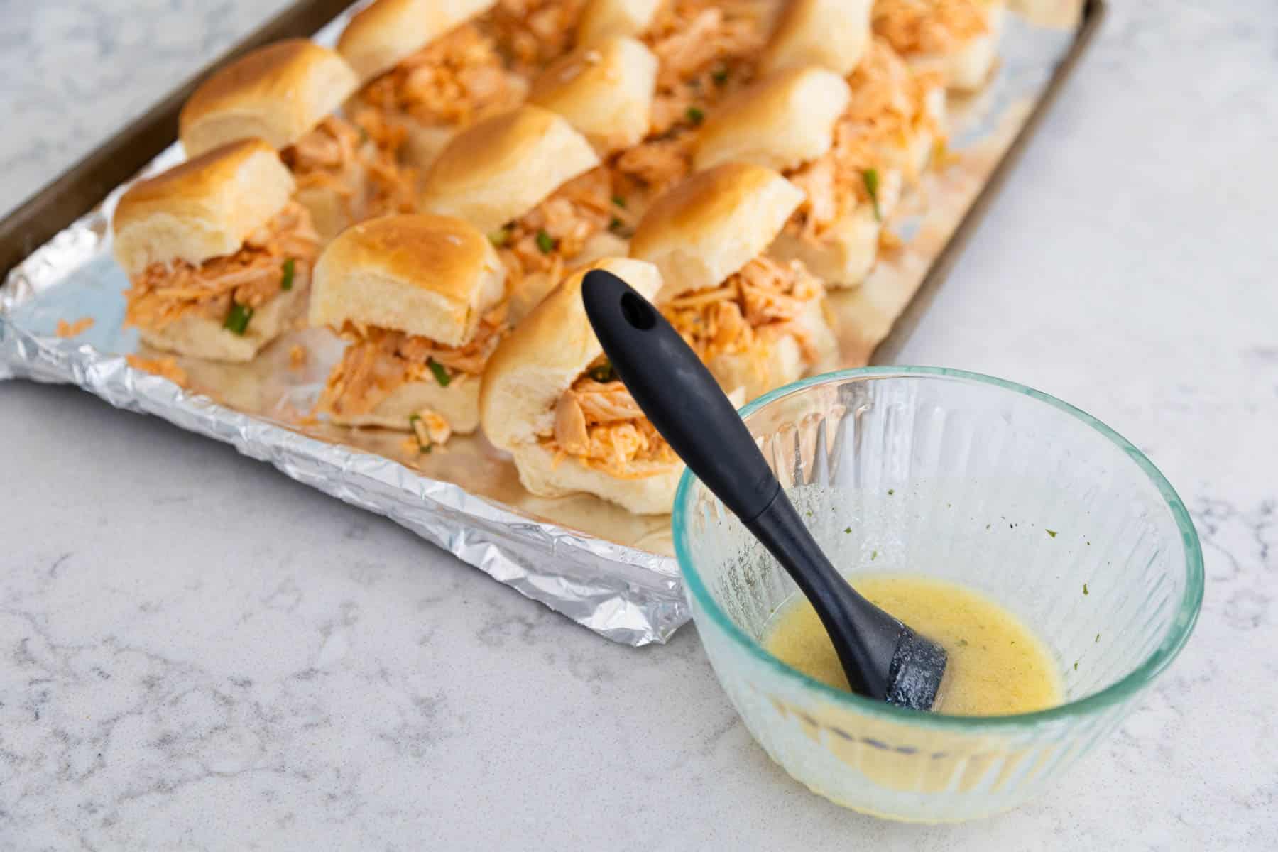 The melted butter mixed with ranch seasoning is being brushed over the slider tops.