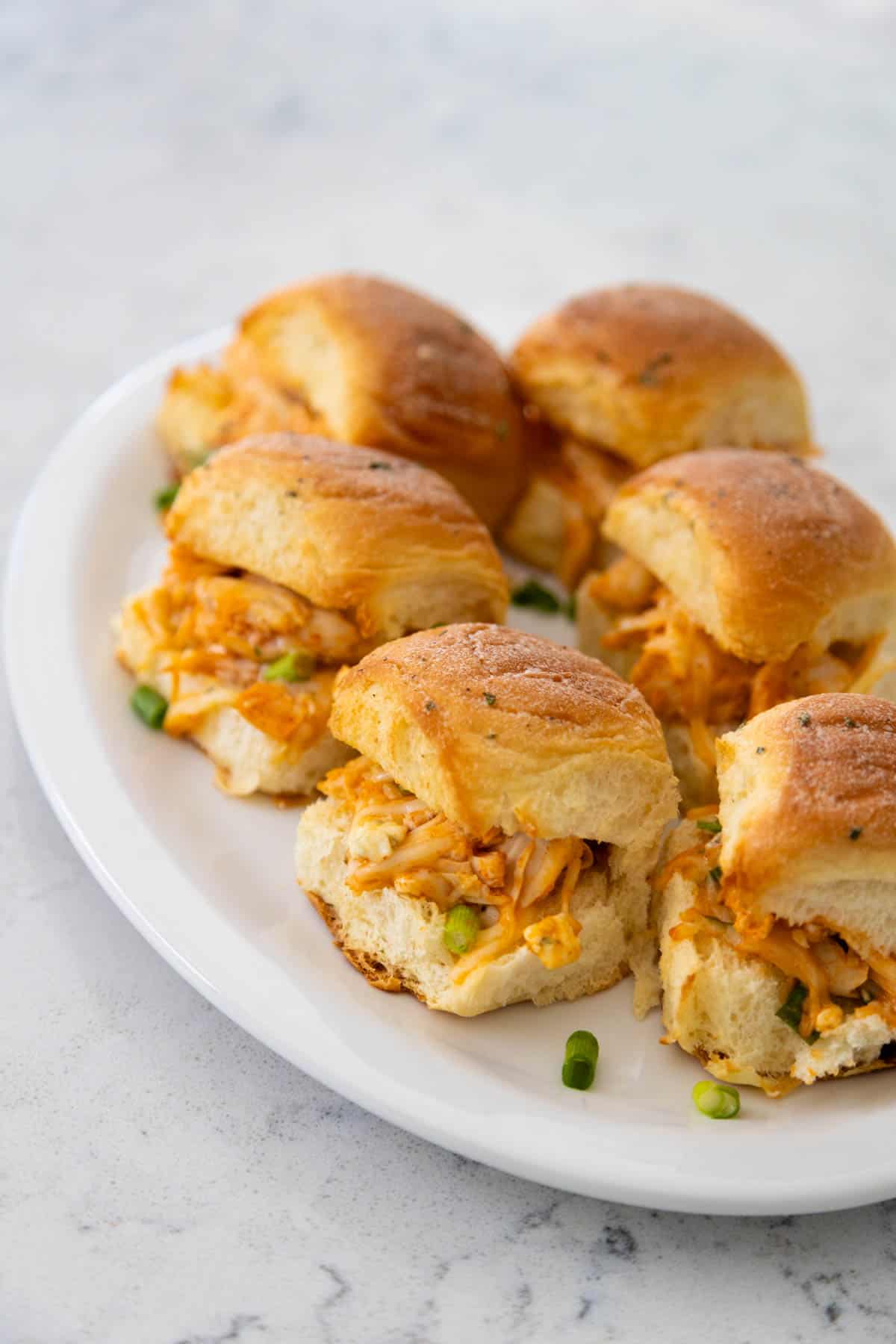 A white serving platter has several chicken sliders on it.