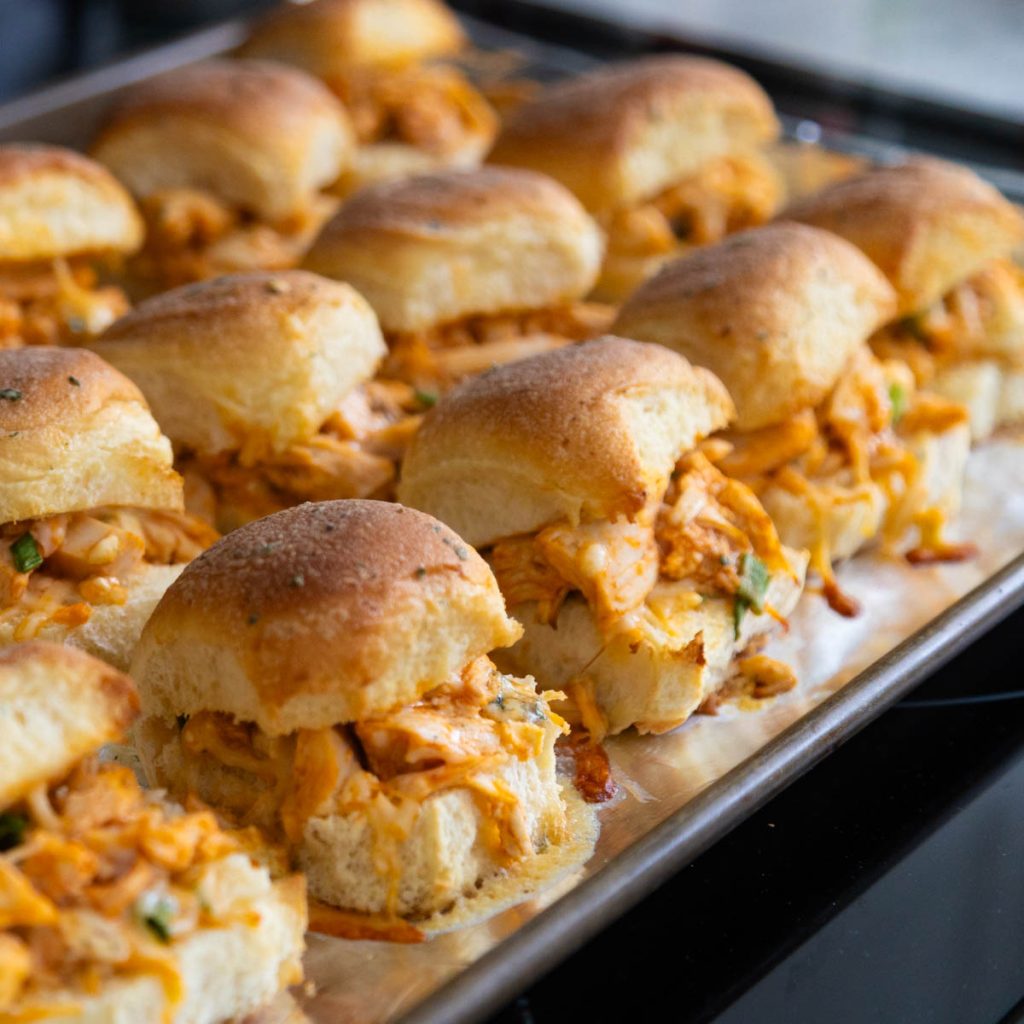 The baking pan of buffalo chicken sliders is sitting on the stovetop, they just came out of the oven.