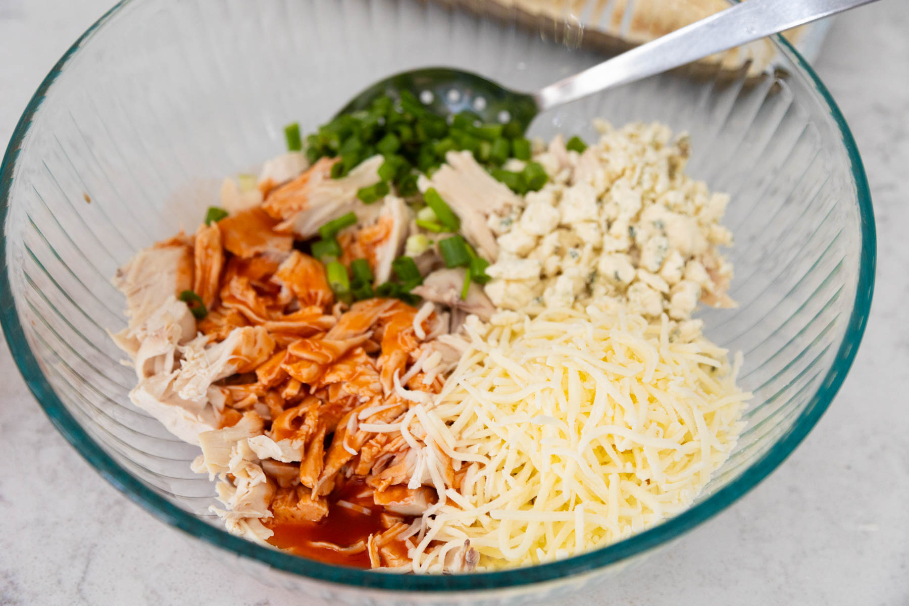 The shredded chicken, buffalo sauce, shredded cheese, and green onions are about to be mixed together in a mixing bowl.