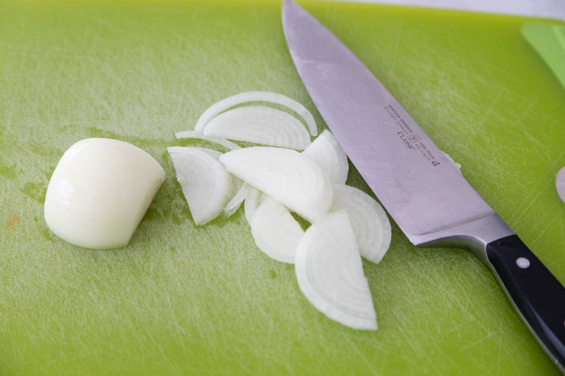 The onions are sliced thinly on a cutting board with a chef knife off to the side.