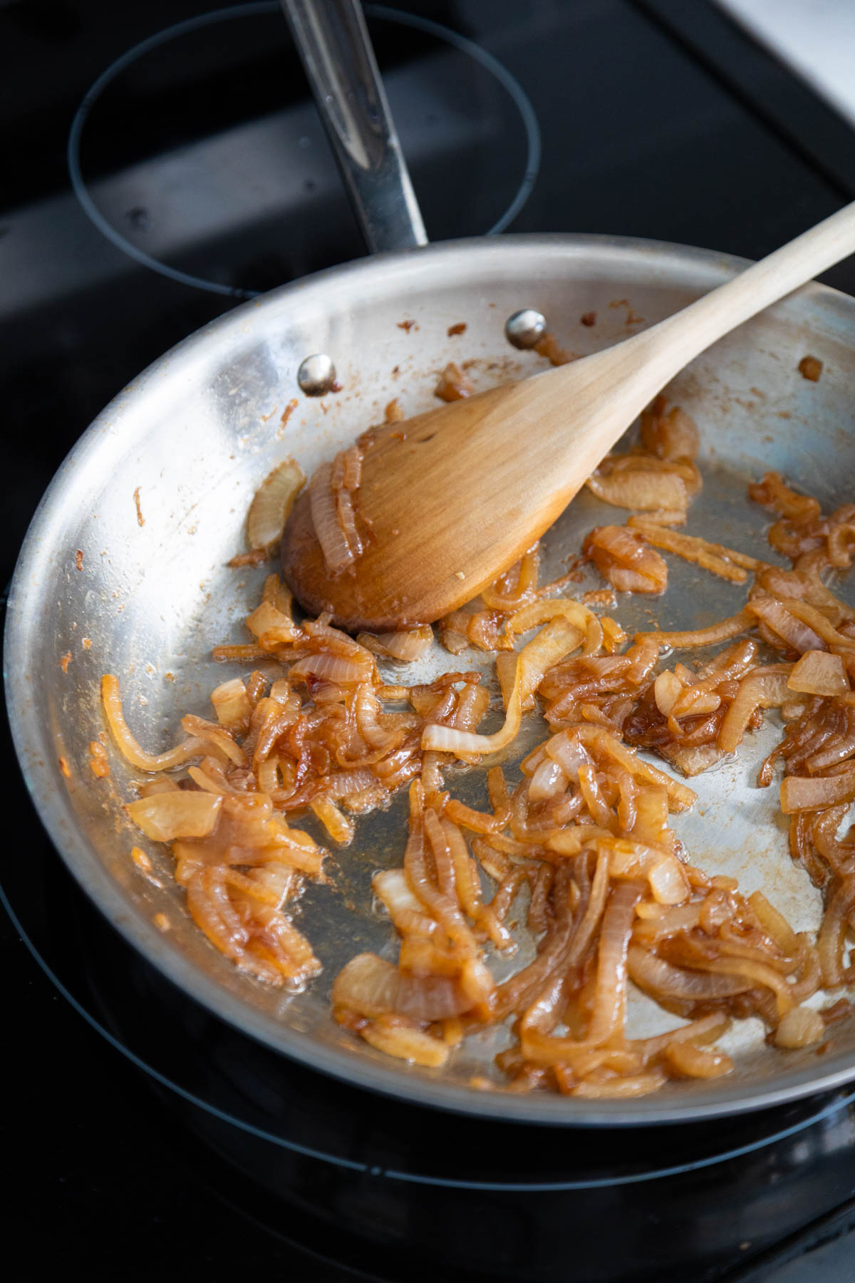 The finished onions are in a skillet being stirred by a wooden spoon.
