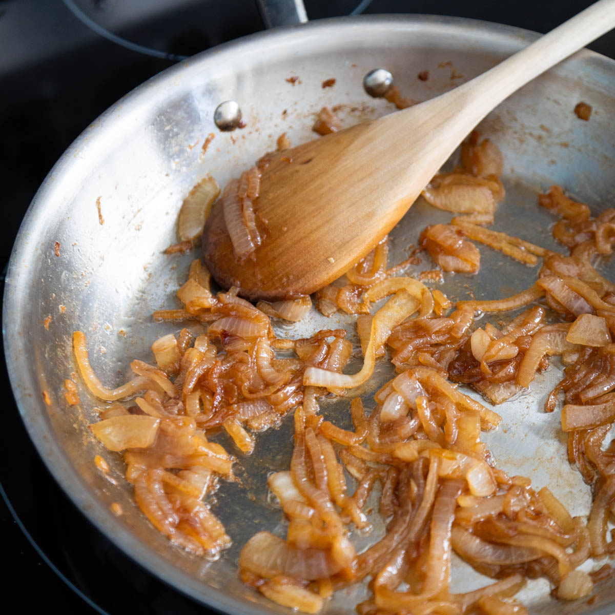 A skillet has caramelized onions being stirred by a wooden spoon.
