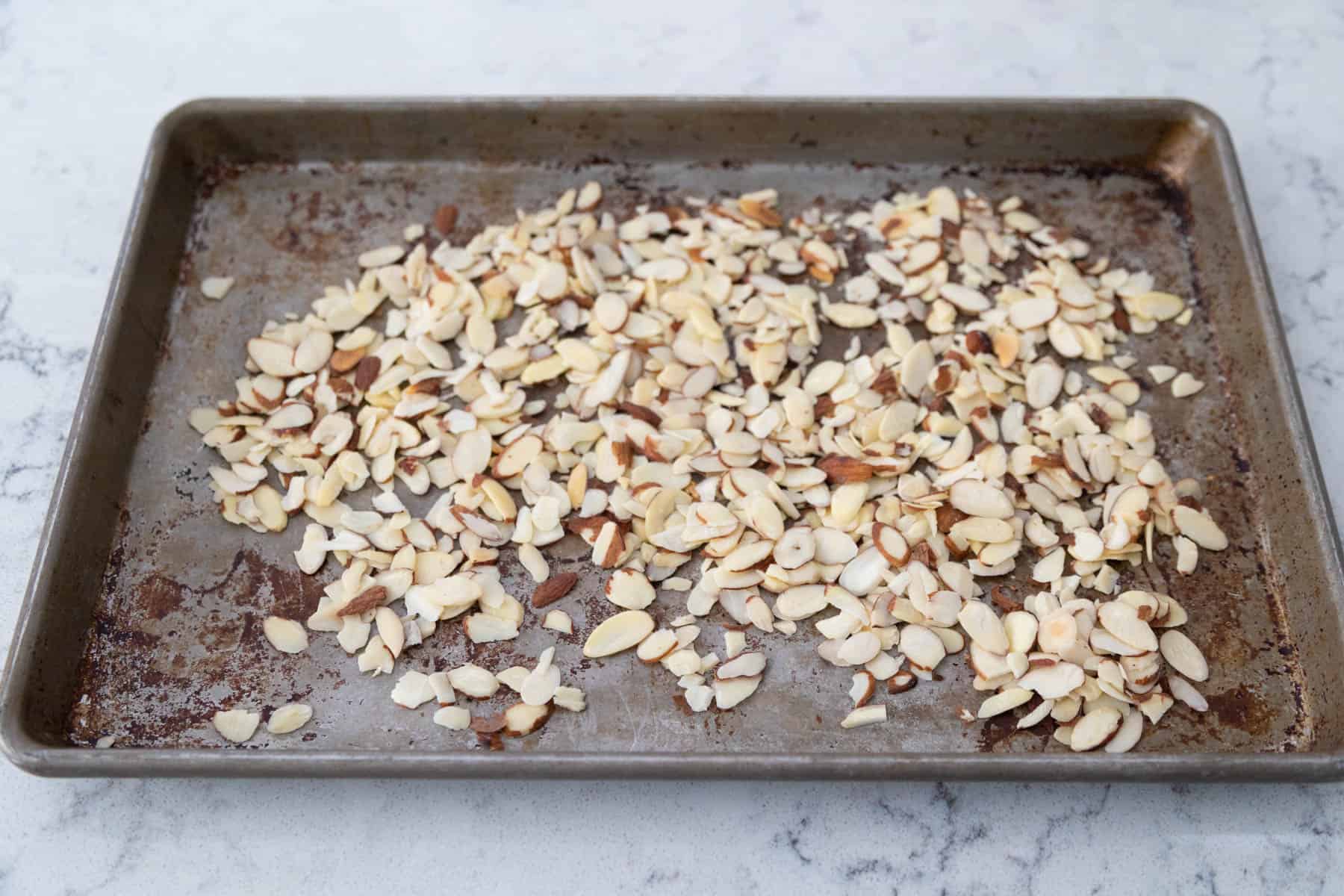 The sliced almonds are spread out on a roasting sheet.