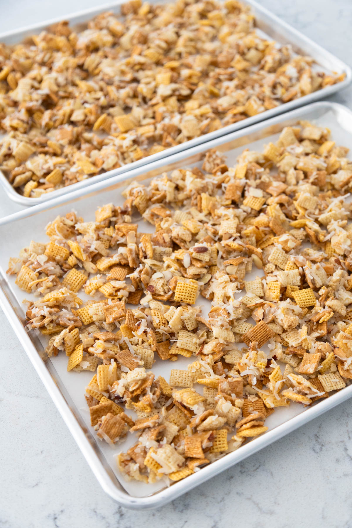 The Chex Mix has finished cooling on the large baking sheets and is ready to be served.