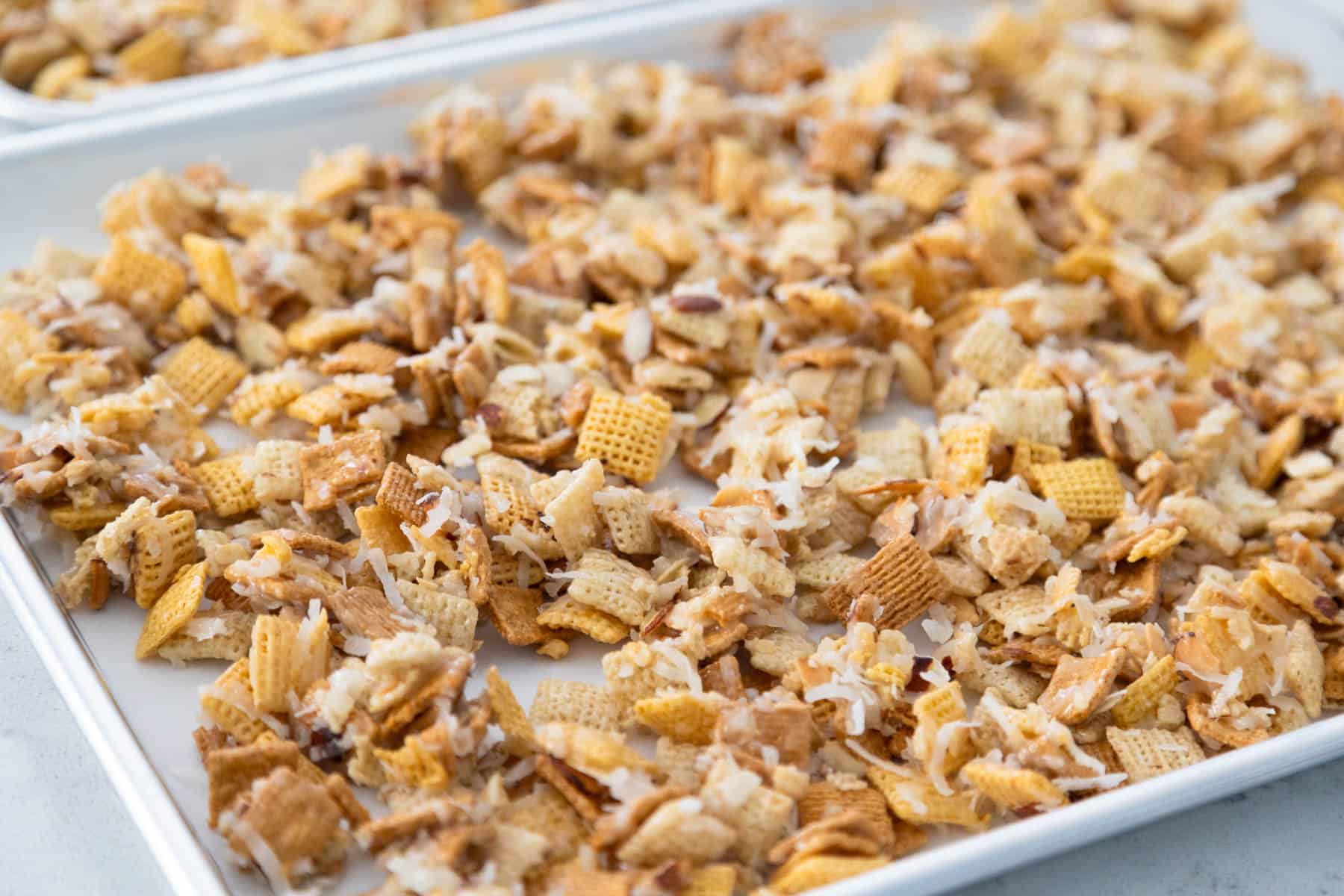 The chex mix is cooling on a baking pan.