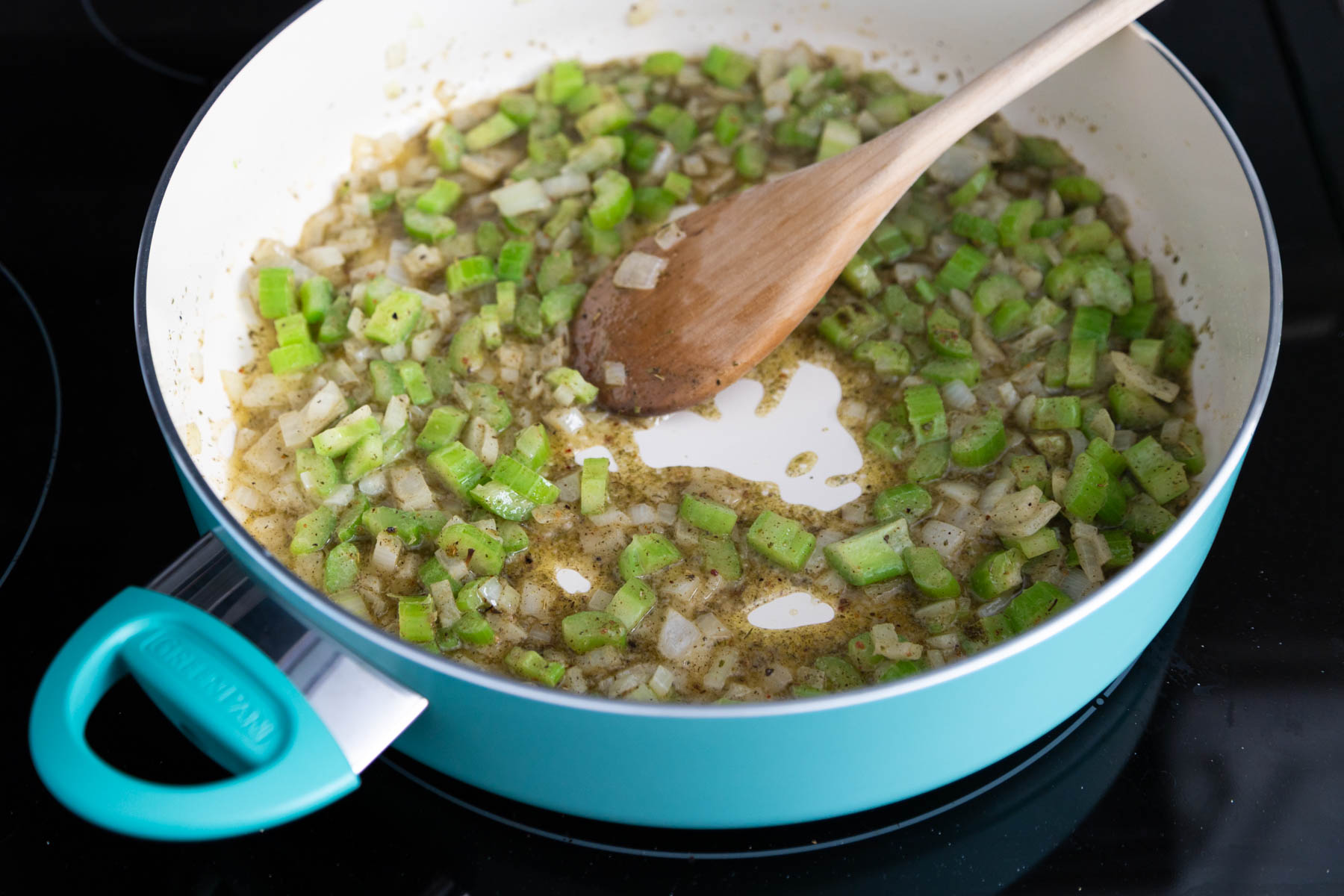 The chopped onion and celery are cooking in a skillet with melted butter.